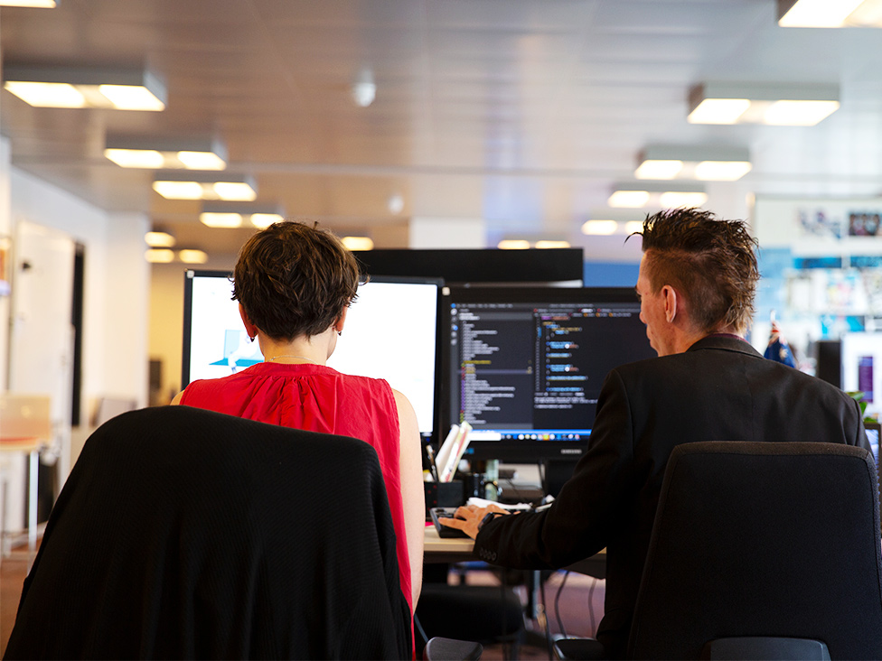 Foto von zwei Debitoor-Mitarbeitern, die an einem Computer sitzen und zusammenarbeiten